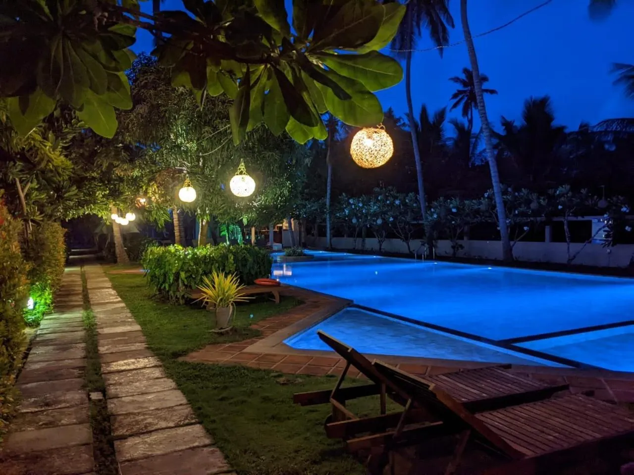 Une piscine illuminée au crépuscule, bordée de végétation et de transats.