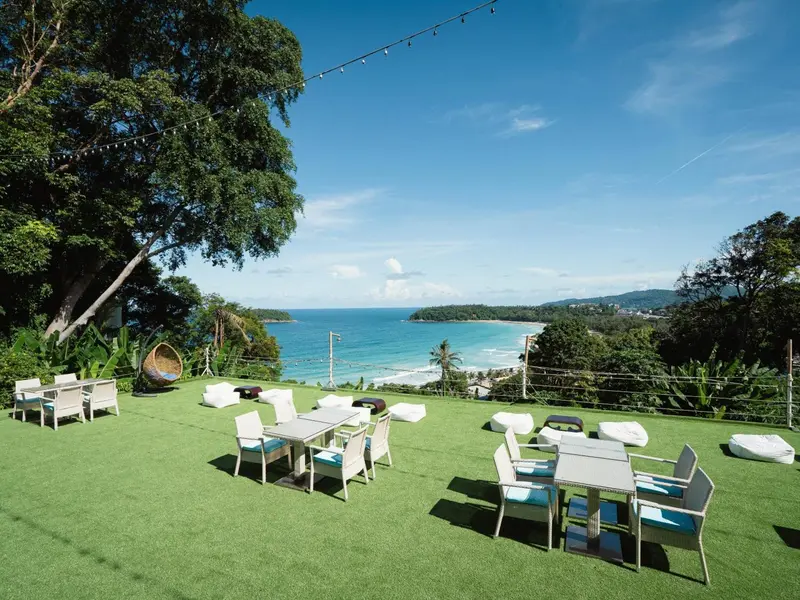 Terrasse verdoyante avec tables et chaises offrant une vue sur la mer et la côte.