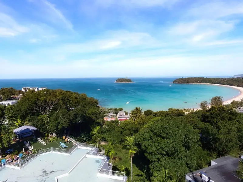 Vue aérienne d'une plage bordée de végétation luxuriante et d'une mer turquoise.