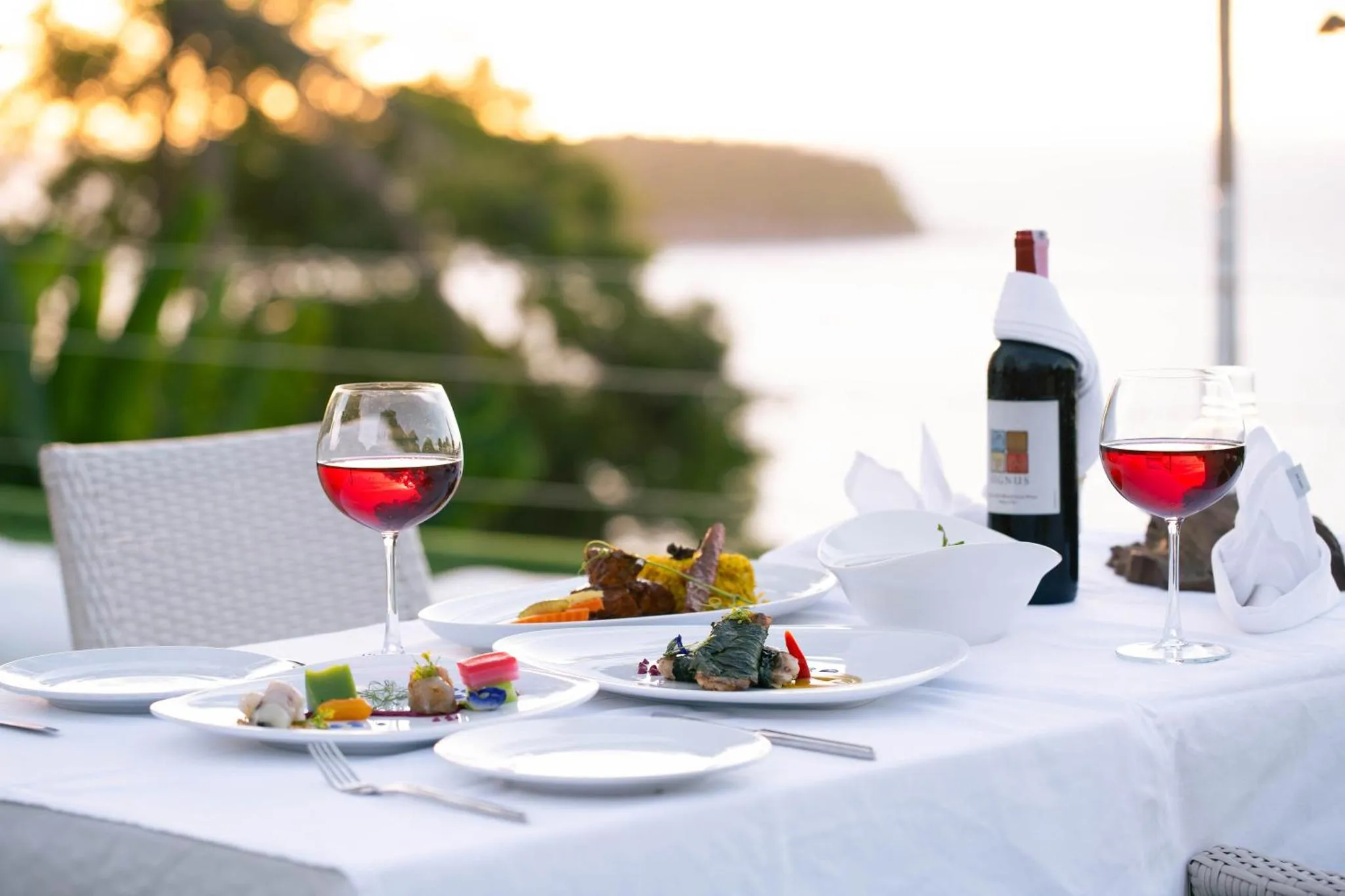 Une table dressée avec des plats et des verres de vin en extérieur, face à la mer.
