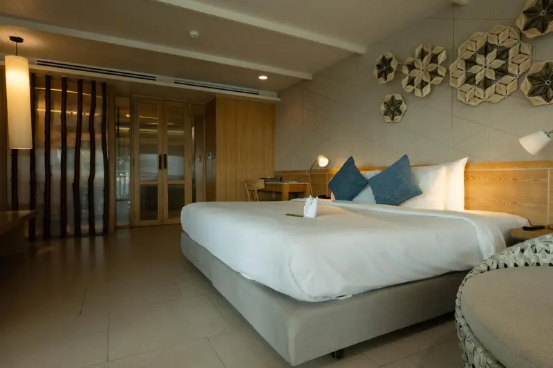 Une chambre lumineuse avec un grand lit recouvert de blanc et des coussins bleus.