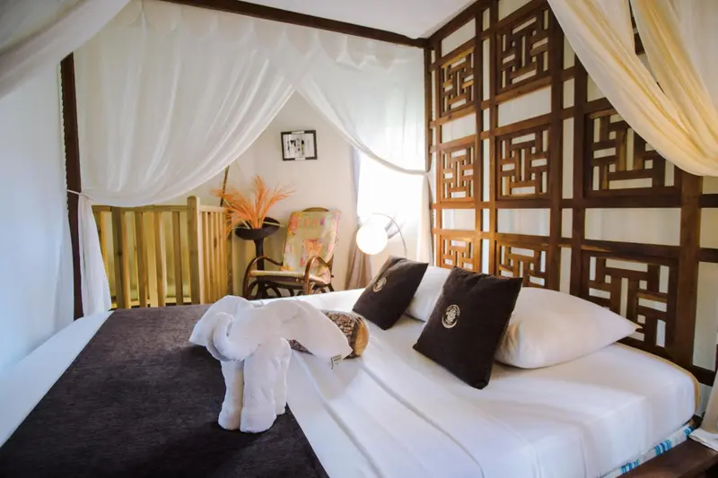 Un lit recouvert de draps blancs et de coussins noirs dans une chambre décorée de bois et de tissus blancs.