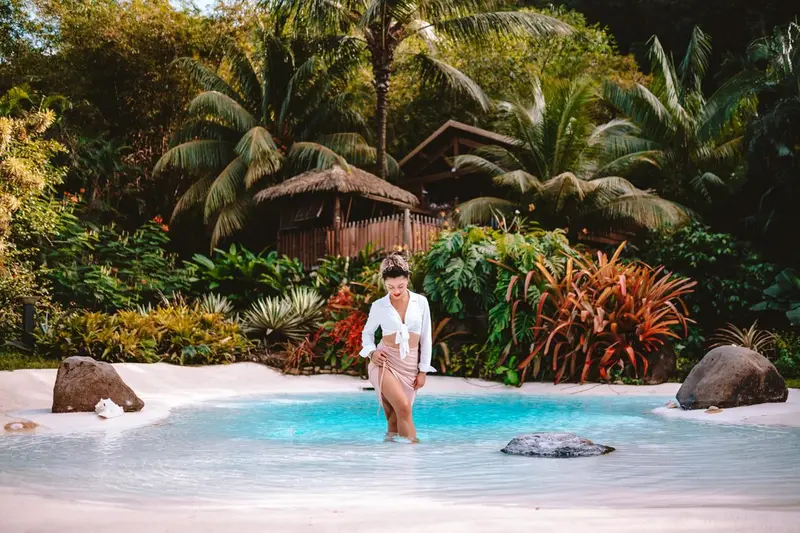 Une femme se tient dans une piscine turquoise entourée de végétation luxuriante.