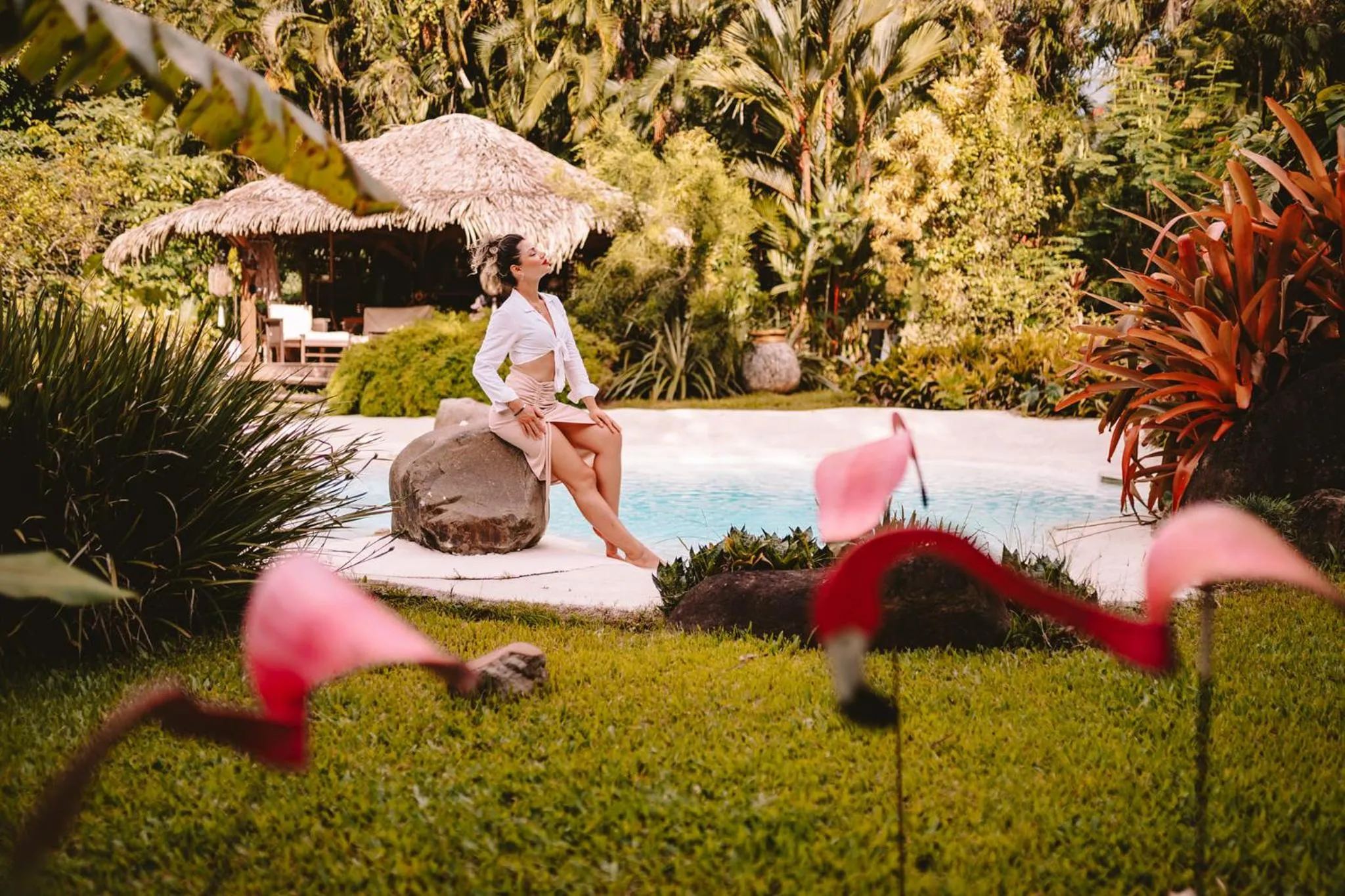 Une femme assise au bord d'une piscine dans un jardin tropical.