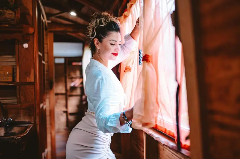 Une femme regarde par une fenêtre dans une pièce au décor rustique.