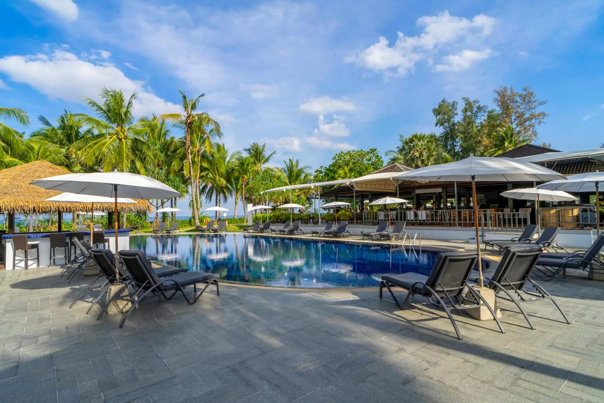 Transats et parasols bordent une piscine turquoise dans un cadre tropical.