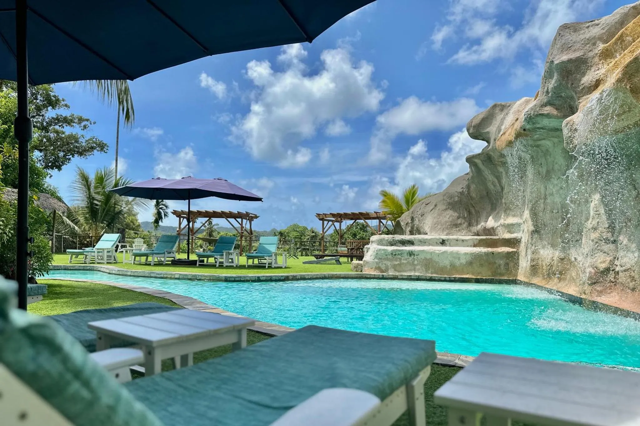 Transats et parasols bordent une piscine turquoise au milieu d'une végétation luxuriante.
