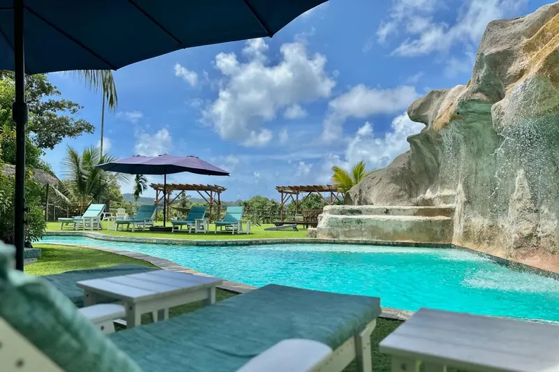 Transats et parasols bordent une piscine turquoise au milieu d'une végétation luxuriante.