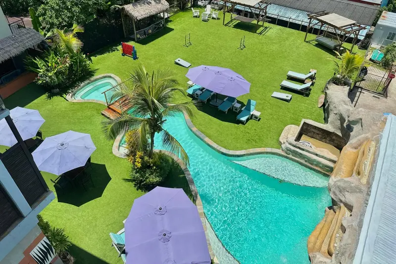 Espace extérieur avec piscine sinueuse et parasols colorés sur une pelouse verdoyante.