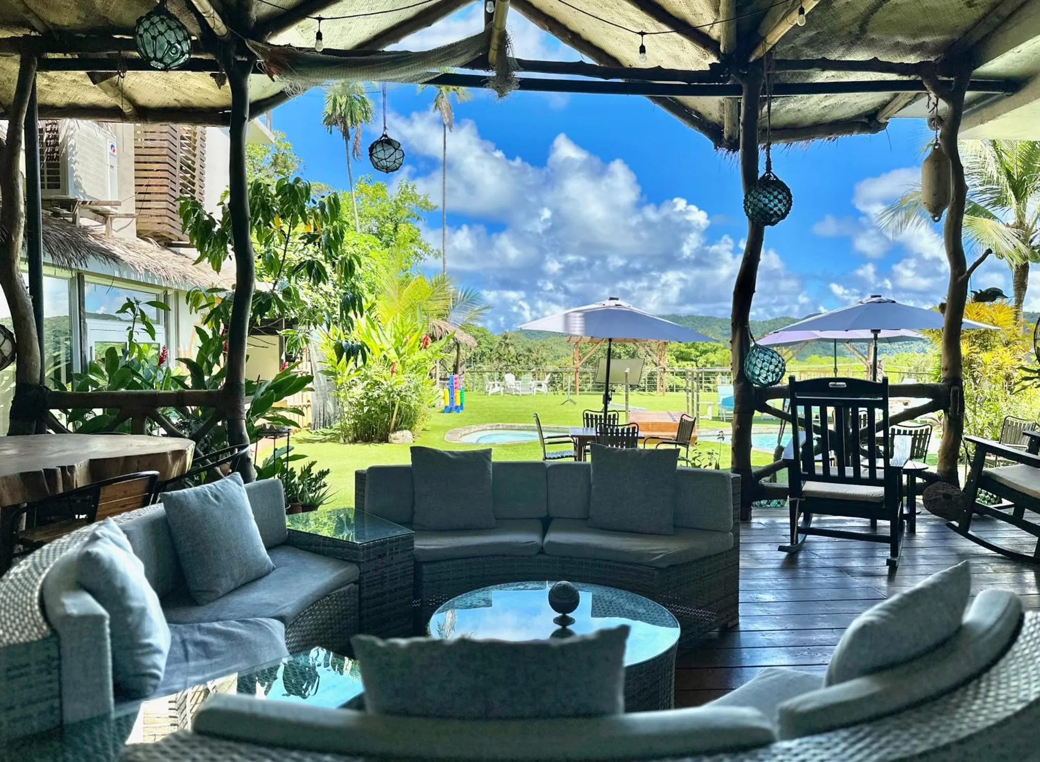Espace de détente extérieur avec canapés et vue sur une piscine et un jardin tropical.