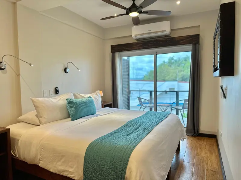Une chambre lumineuse avec un grand lit recouvert d'une courtepointe turquoise et un accès à un balcon.