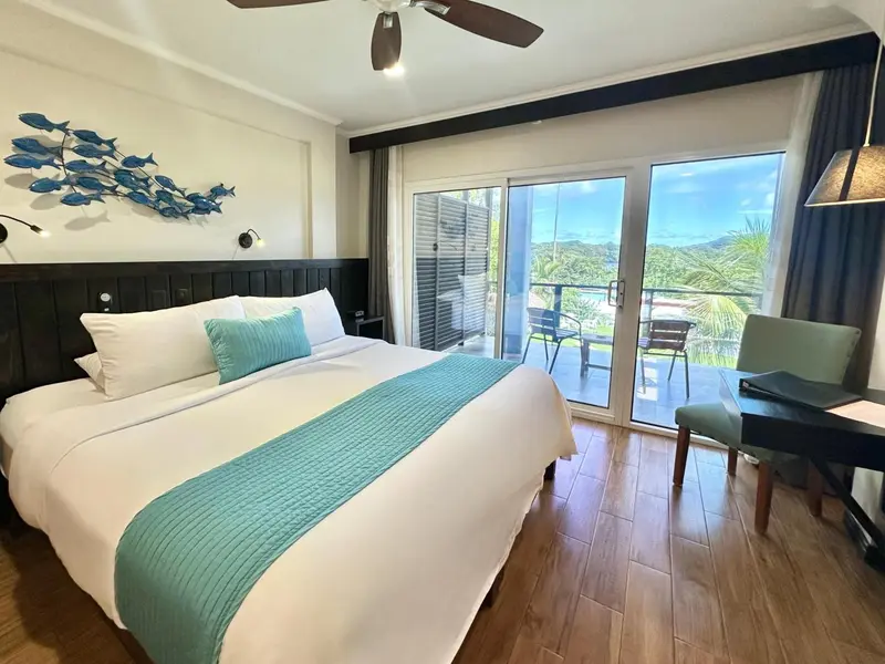 Une chambre lumineuse avec un lit recouvert d'une courtepointe turquoise et une vue sur une terrasse.