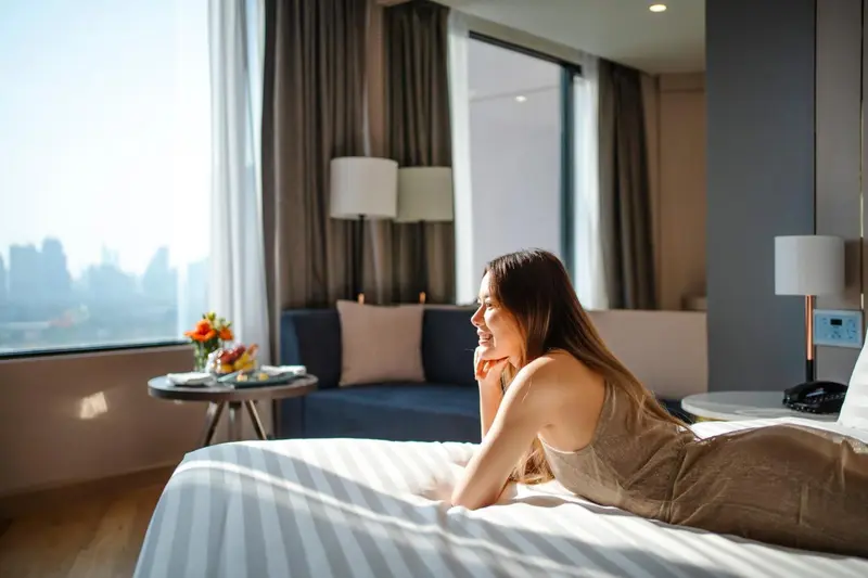 Une femme se repose sur un lit dans une chambre avec vue sur la ville.