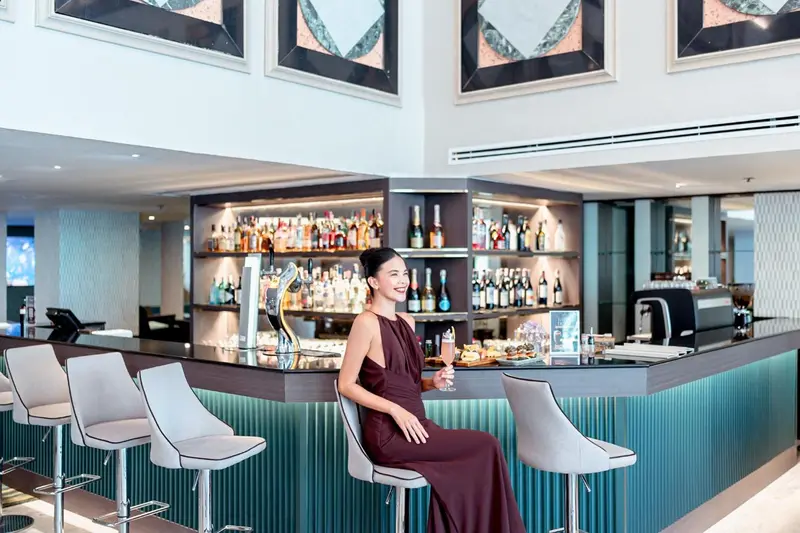 Une femme souriante est assise au comptoir d'un bar moderne et élégant.