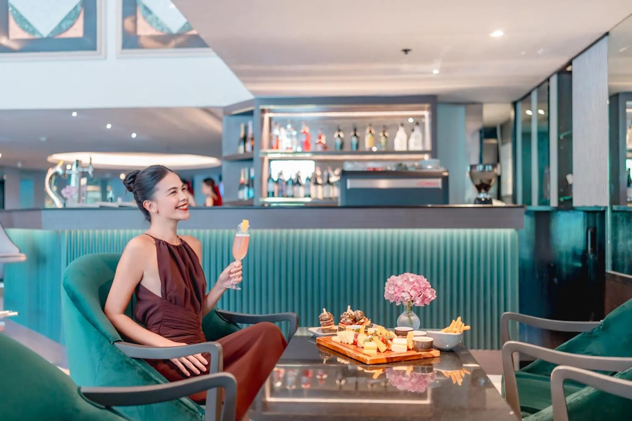 Une femme souriante est assise près d'un comptoir de bar avec une boisson et des amuse-gueules.