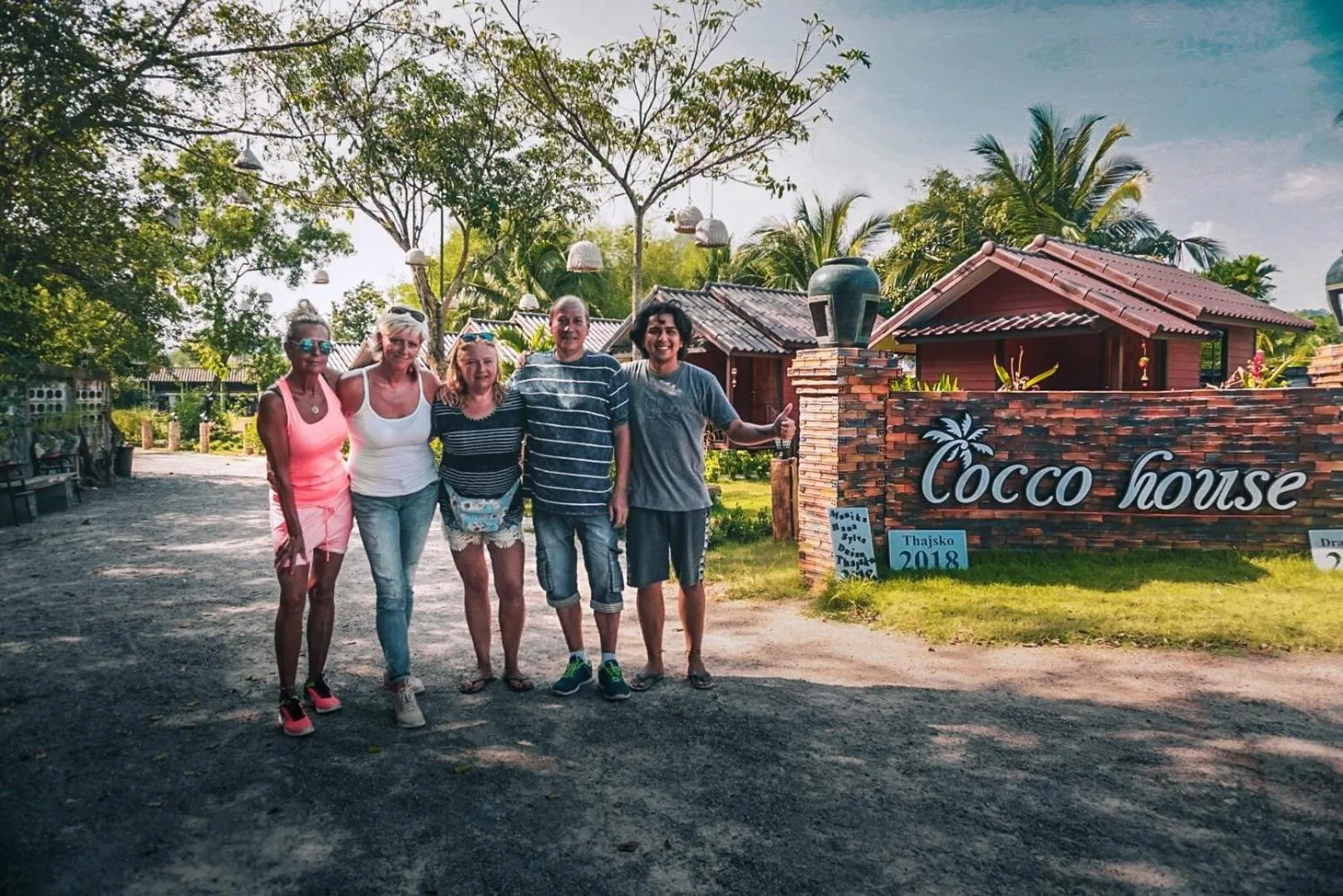 Quatre personnes sourient devant un bâtiment et une végétation tropicale.