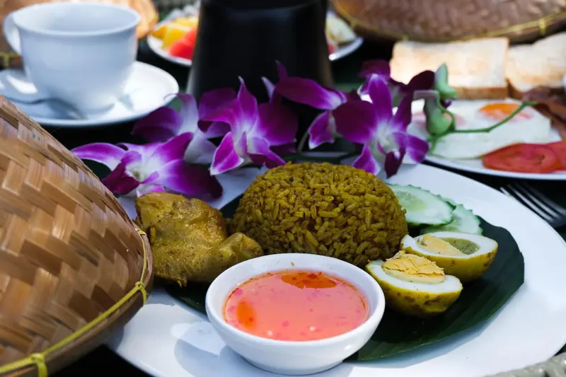 Une table est dressée avec un repas composé de riz, de viande, d'œufs et de légumes.