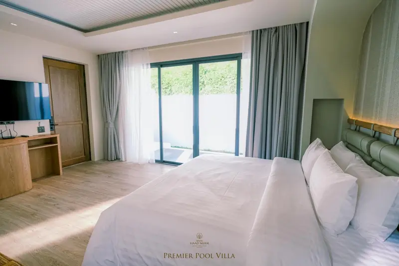 Une chambre lumineuse avec un grand lit recouvert de draps blancs et des rideaux verts.