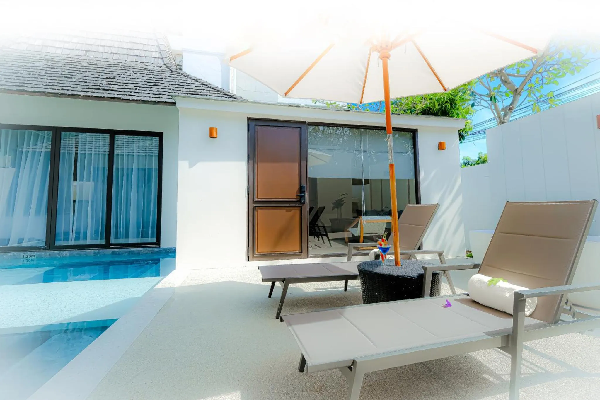 Terrasse avec transats devant une maison blanche et une piscine.