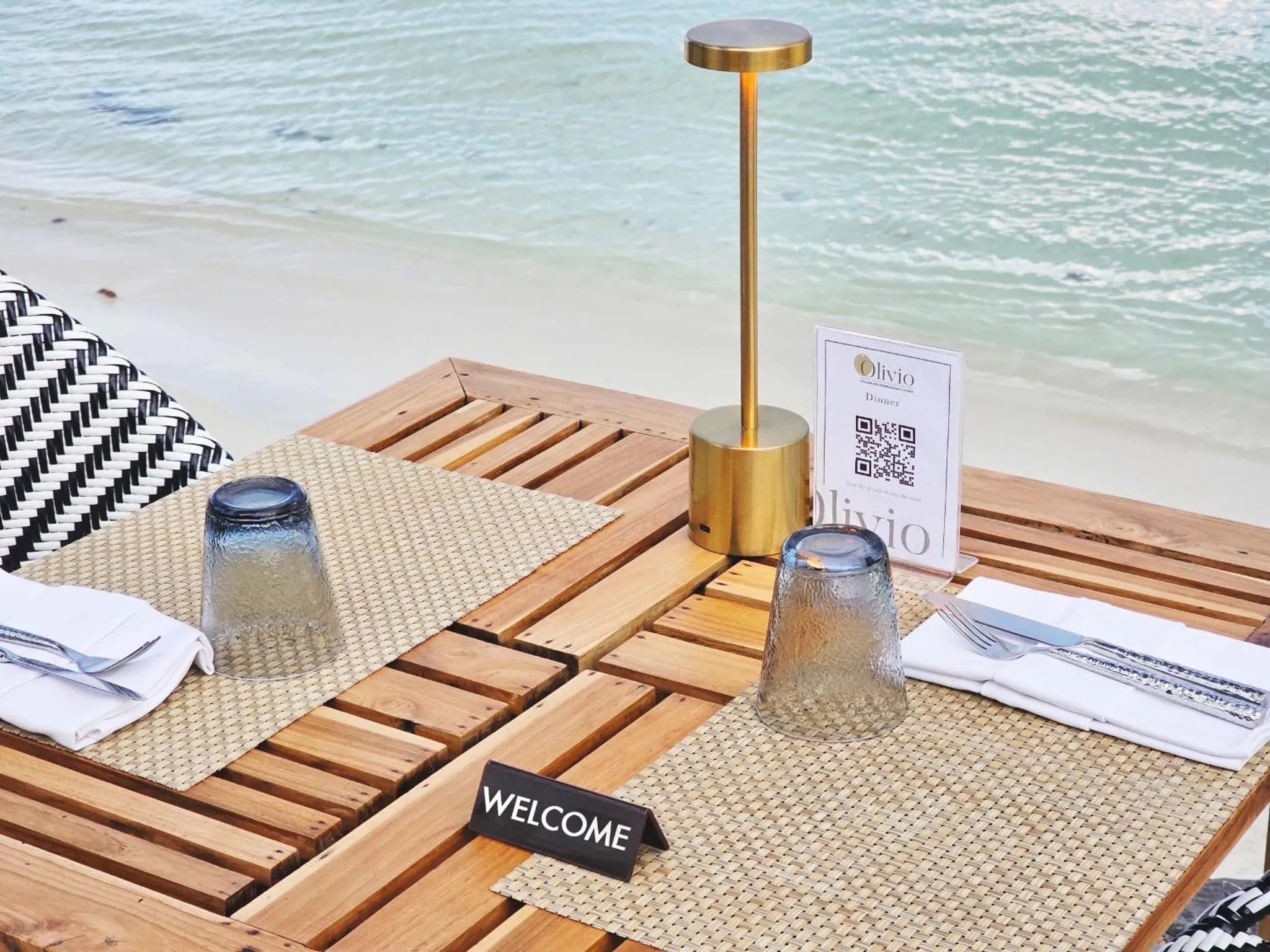 Table basse en bois avec couverts et verres sur une plage de sable blanc.