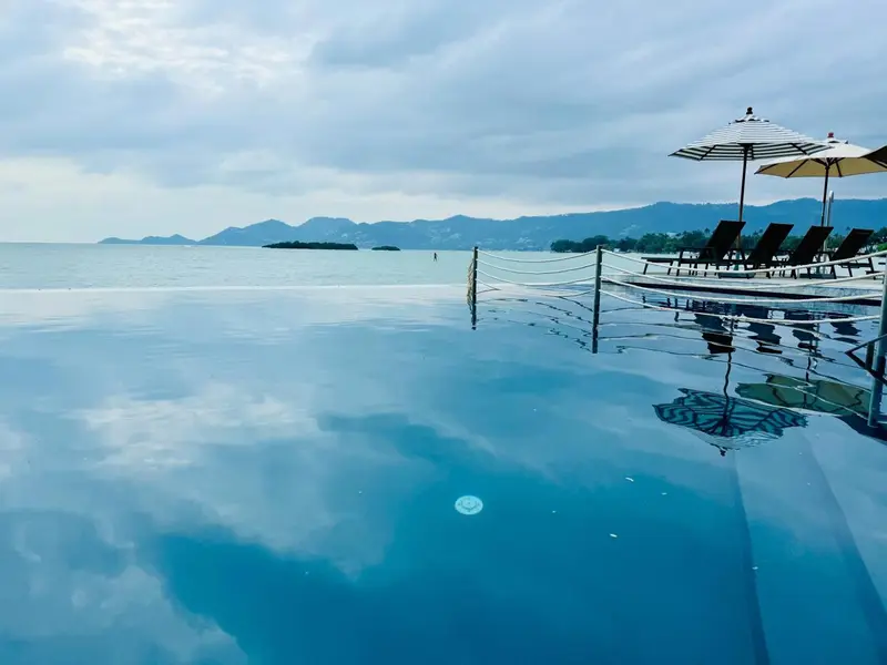 Transats blancs disposés au bord d'une piscine à débordement face à la mer.