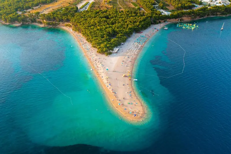 Vue aérienne d'une plage de sable fin bordée d'eaux turquoise et de végétation luxuriante.