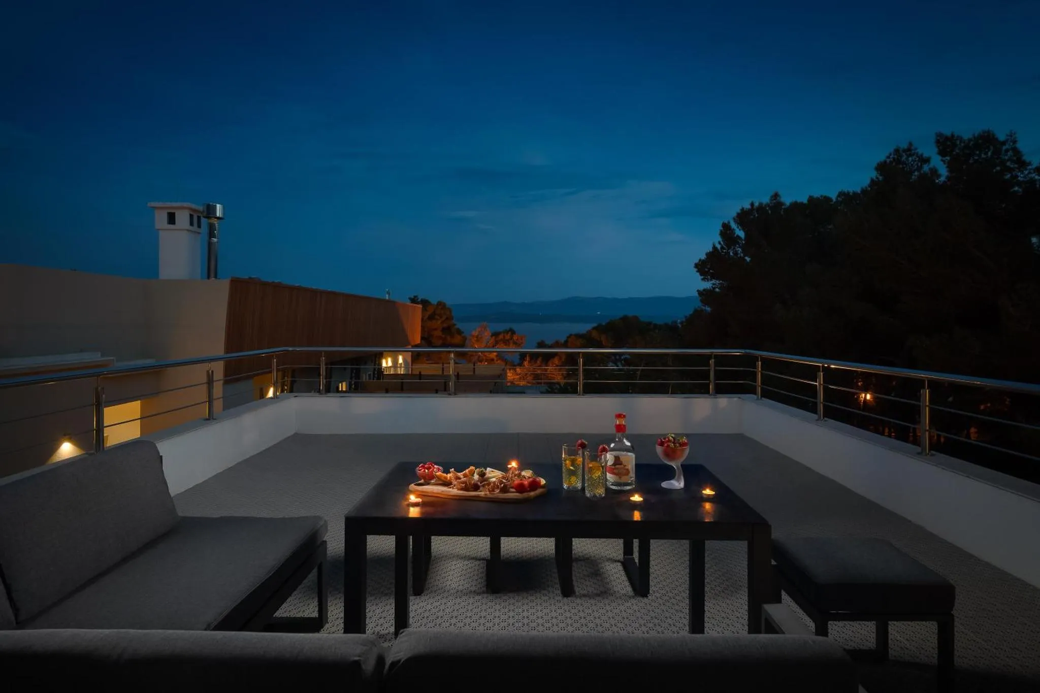 Une table basse avec des boissons et des amuse-gueules est mise en scène sur une terrasse éclairée.