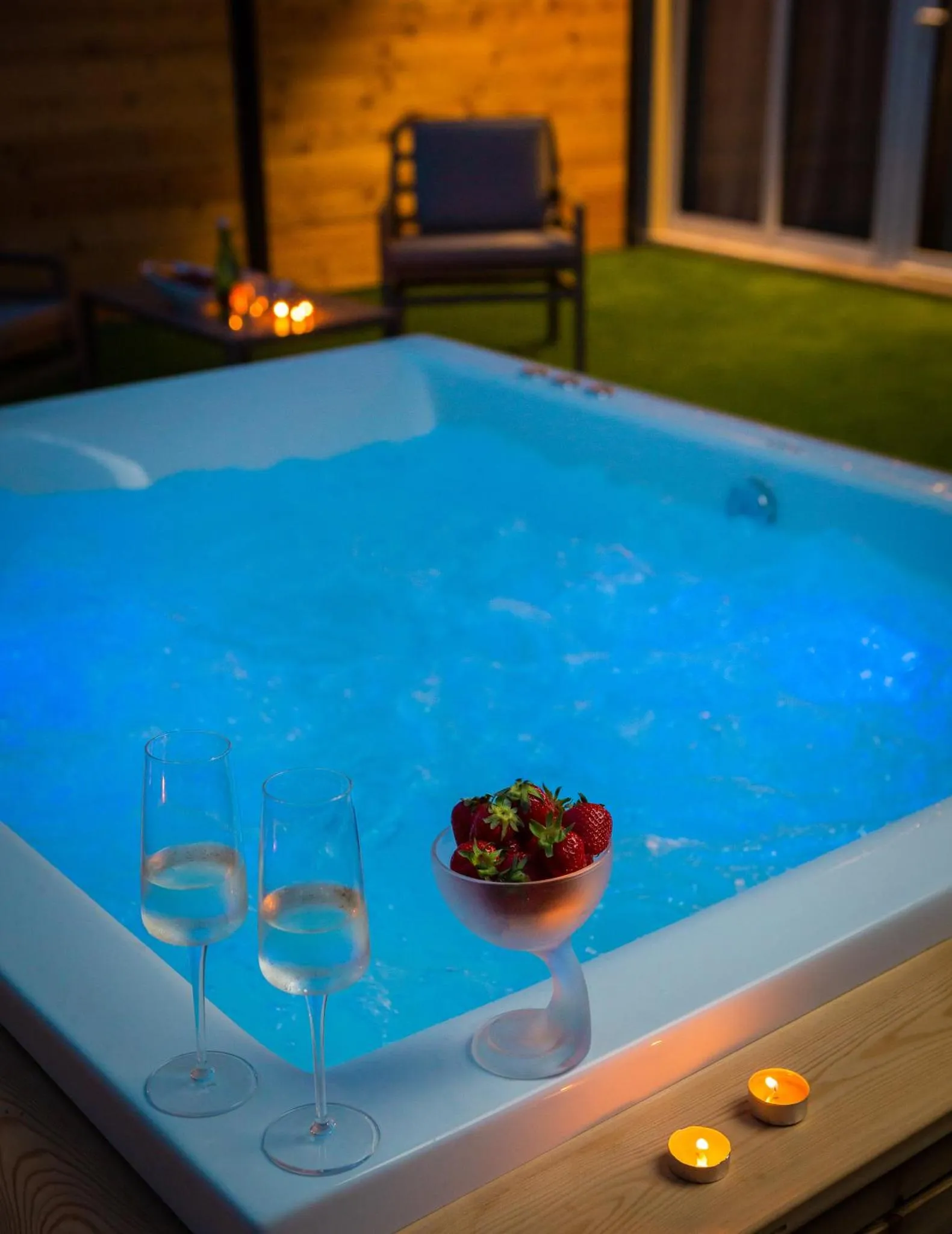 Un jacuzzi illuminé avec des verres et des fraises, sur une terrasse.
