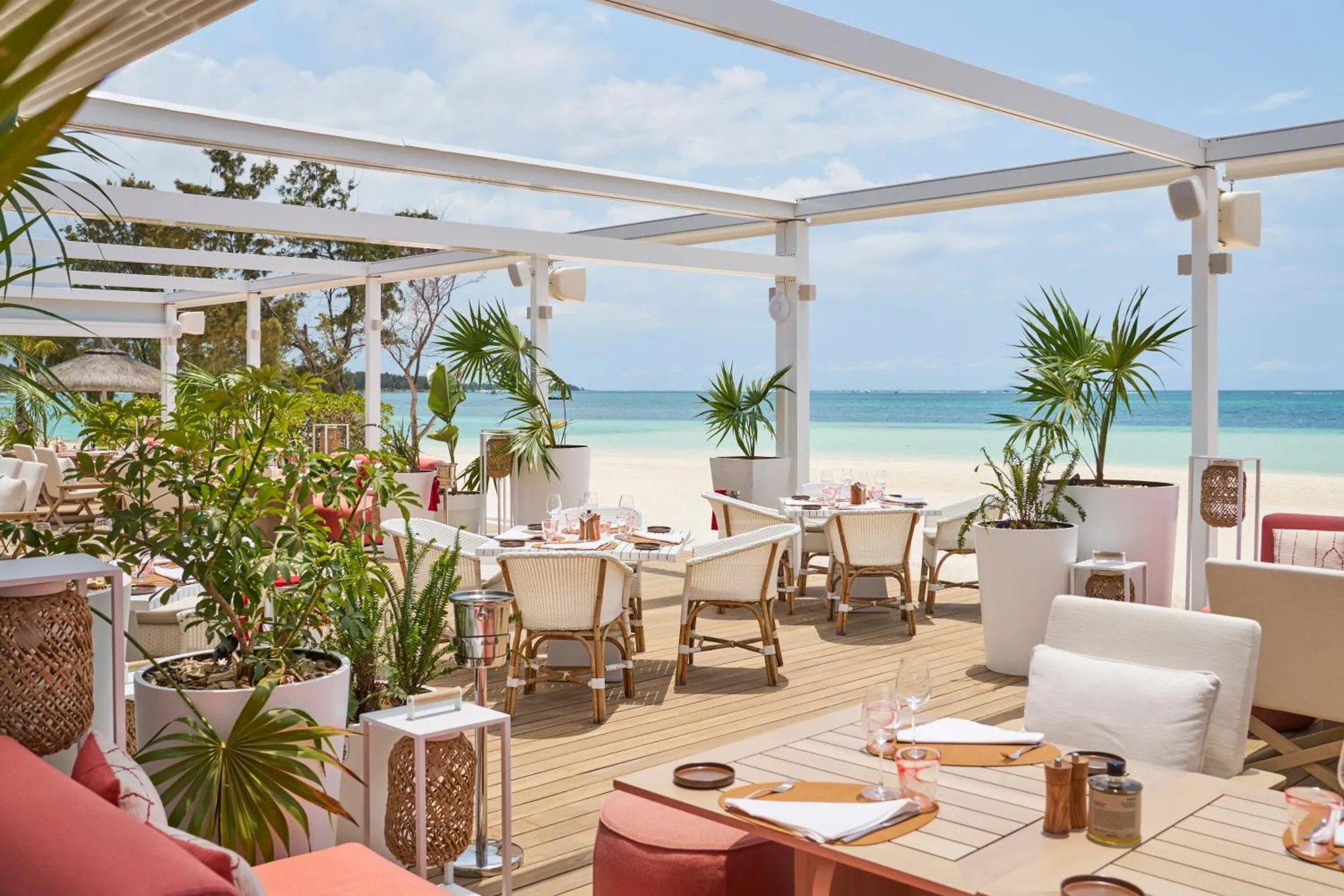 Terrasse ombragée avec tables dressées face à une plage de sable blanc.