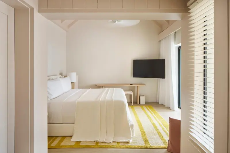 Chambre lumineuse avec un lit recouvert d'une couverture blanche et un tapis jaune.