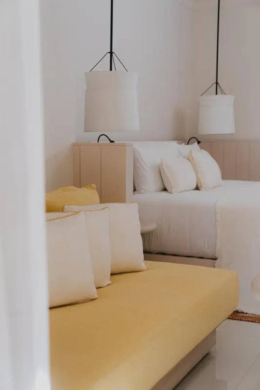 Une chambre lumineuse avec un lit double et une banquette jaune.