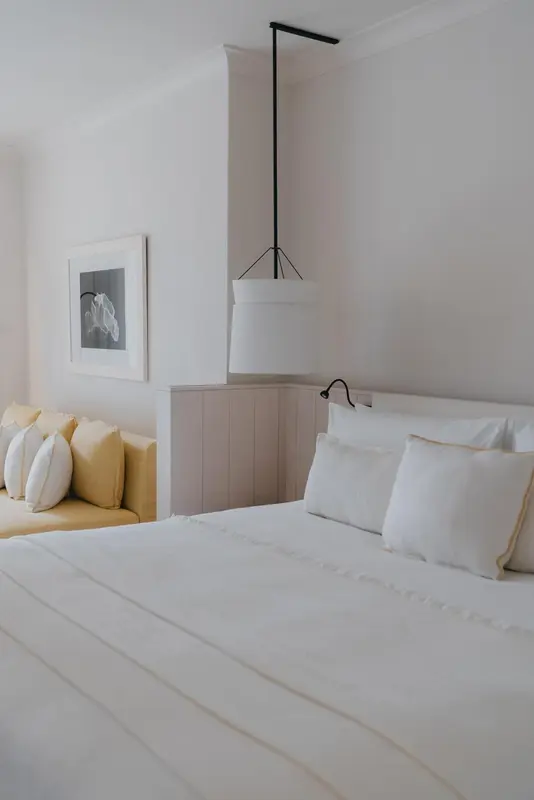 Une chambre lumineuse avec un lit fait et un canape jaune.