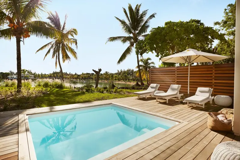 Petite piscine turquoise et transats blancs sur une terrasse en bois.