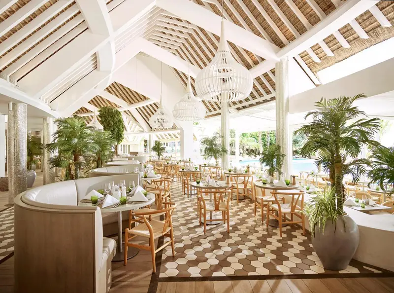 Une salle de restaurant lumineuse avec des tables dressées et une décoration tropicale.