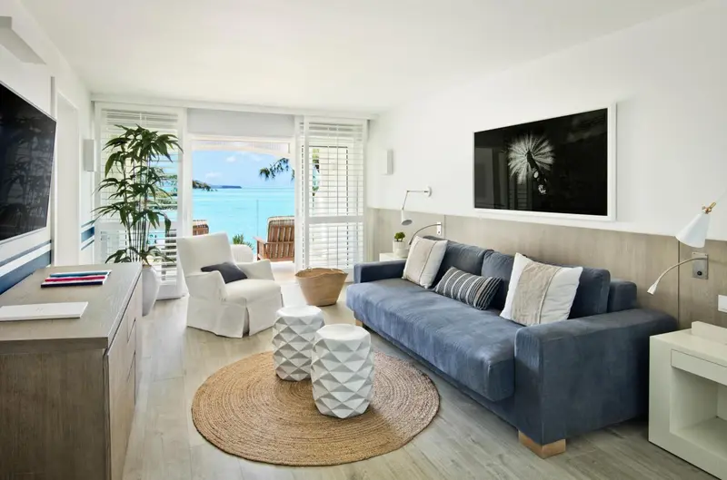 Un salon lumineux avec canapé bleu et fauteuil blanc donne sur une vue mer.