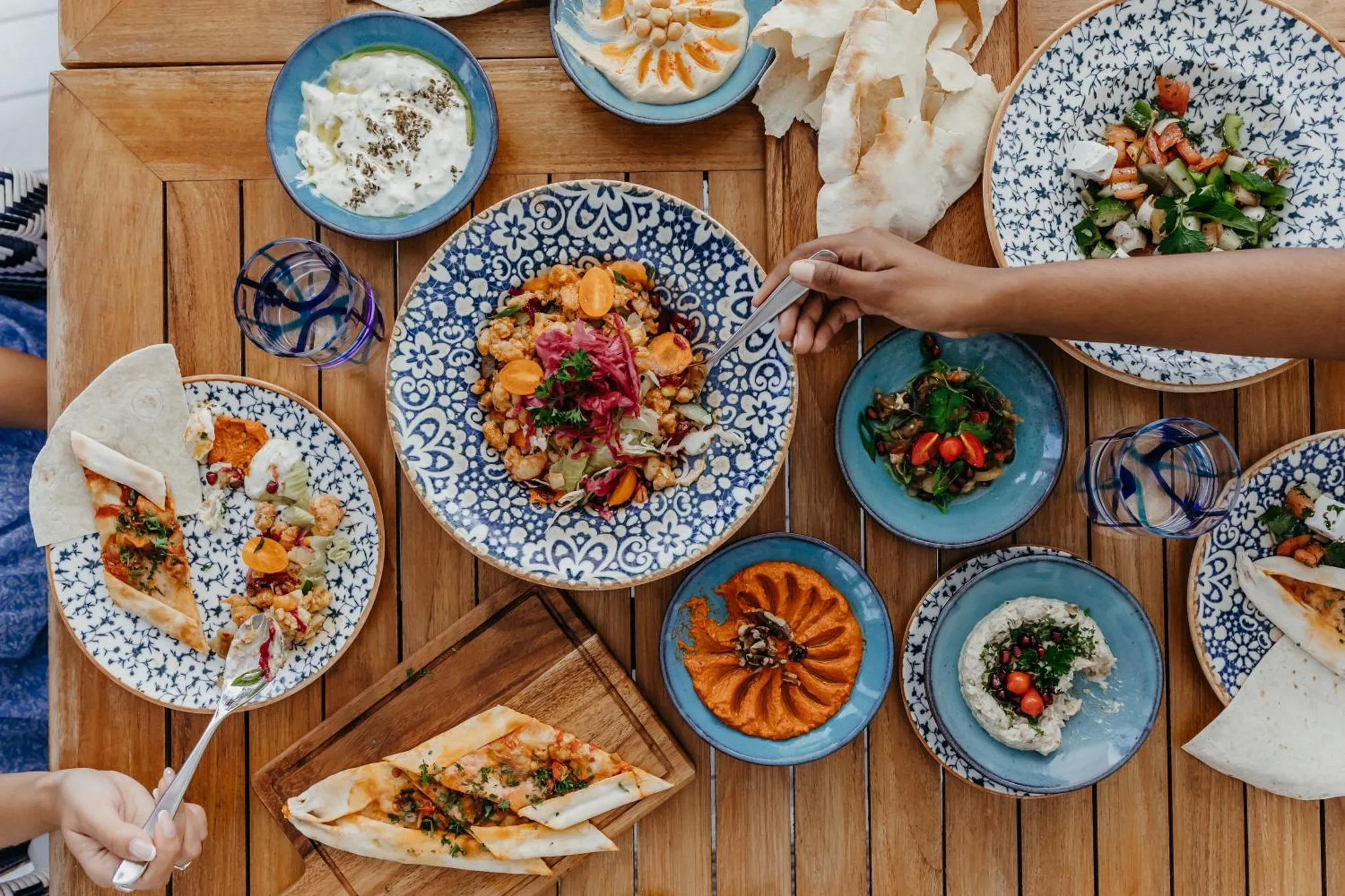 Une table en bois est dressée de divers plats colorés et de pains.