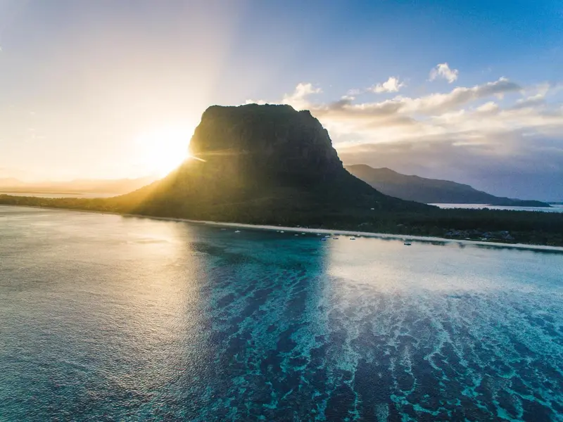 Un paysage côtier avec une montagne rocheuse et une eau turquoise scintillante au soleil.