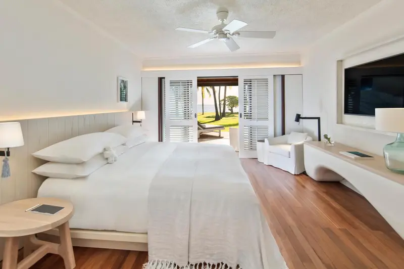 Chambre lumineuse avec un grand lit et vue sur une plage.