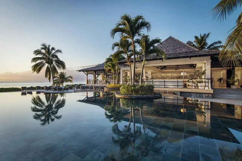 Une piscine à débordement reflète un bâtiment tropical au bord de la mer.