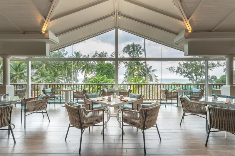Une salle à manger lumineuse s'ouvre sur une vue sur la mer et la végétation.