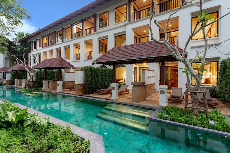 Bâtiment blanc à deux étages avec des balcons et une piscine au premier plan.