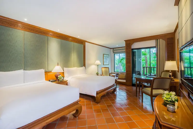 Chambre lumineuse avec deux lits et vue sur une végétation luxuriante.
