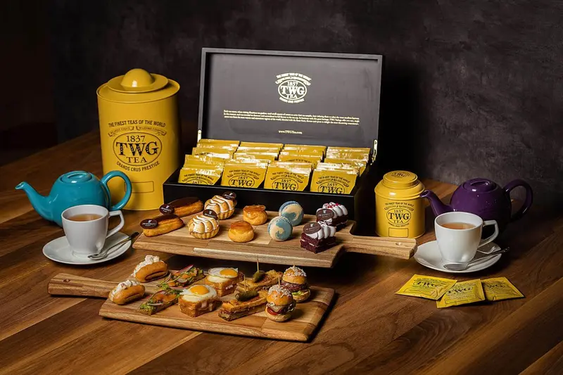 Une table en bois présente une sélection de thés, de pâtisseries et de tasses.