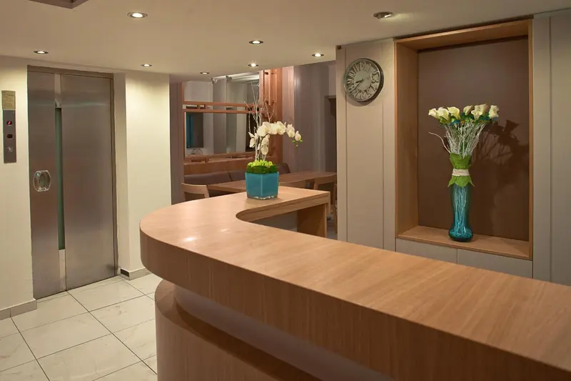 Un comptoir d'accueil en bois clair avec une horloge murale et un arrangement floral.