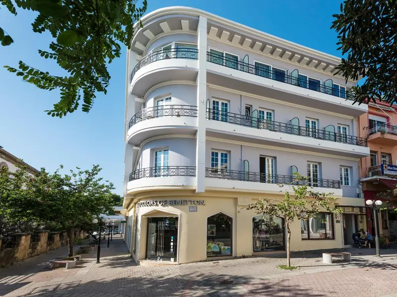 Façade d'un bâtiment blanc à plusieurs étages avec des balcons et des commerces au rez-de-chaussée.