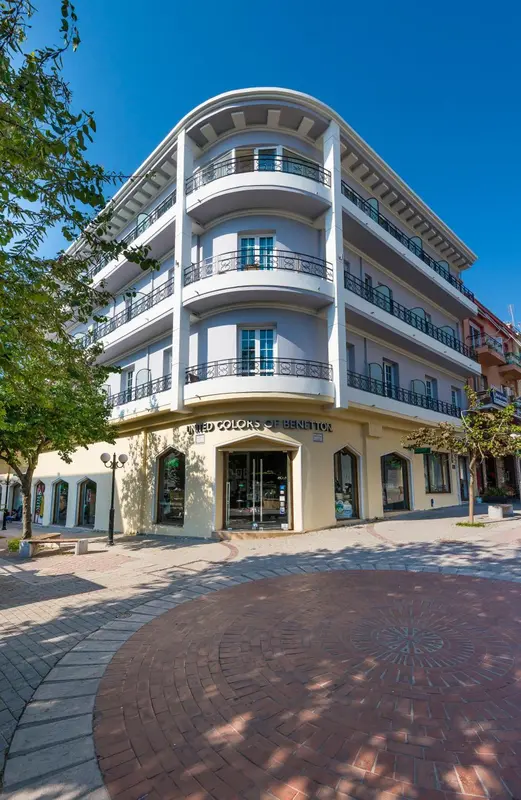 Bâtiment blanc à plusieurs étages avec des balcons et des boutiques au rez-de-chaussée.