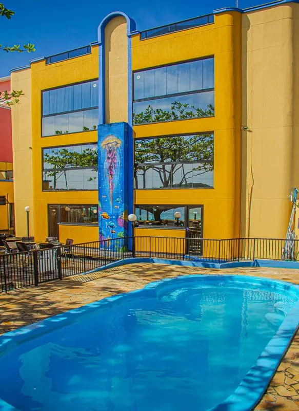 Façade jaune d'un bâtiment avec une piscine au premier plan et une fresque marine.