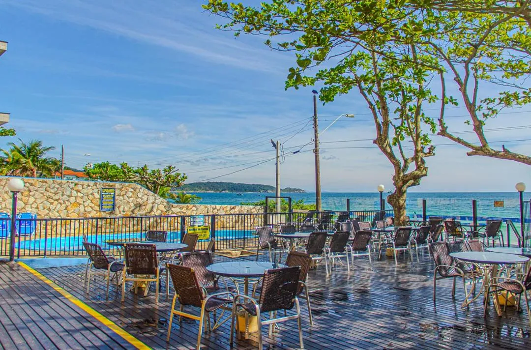 Terrasse avec tables et chaises en bord de mer sous des arbres.