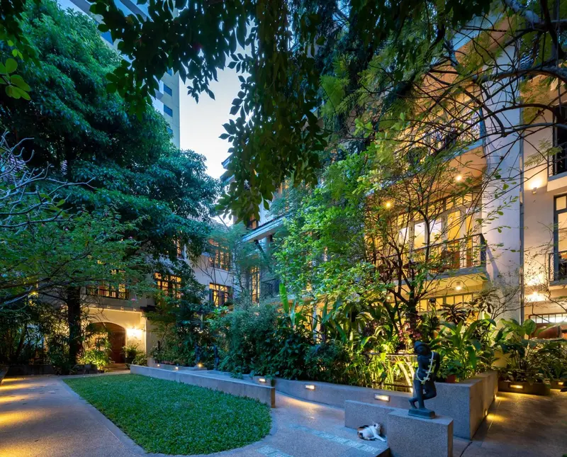 Un jardin luxuriant borde un bâtiment éclairé par des lumières chaudes.