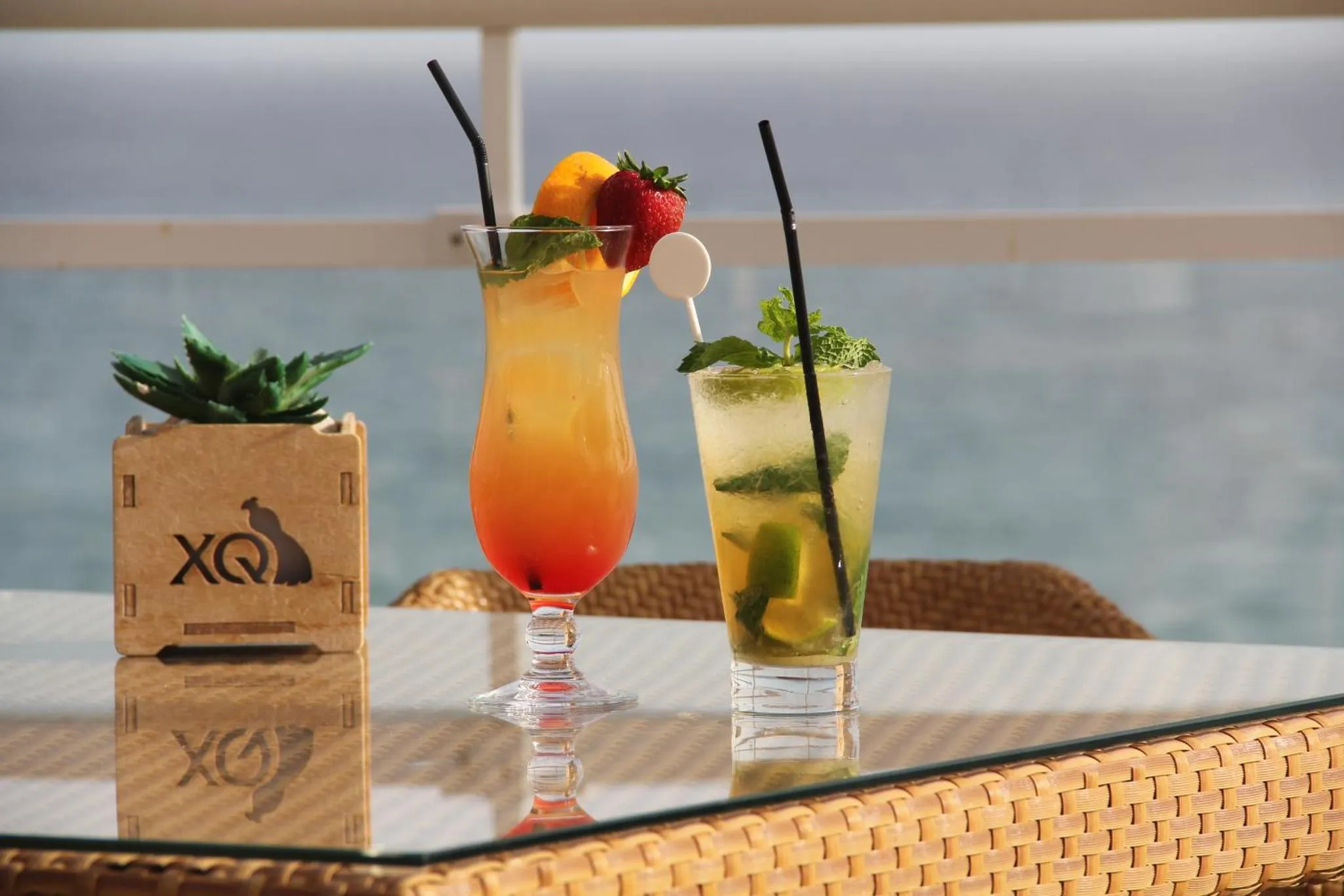 Deux cocktails colorés sont servis sur une table en osier avec vue sur la mer.